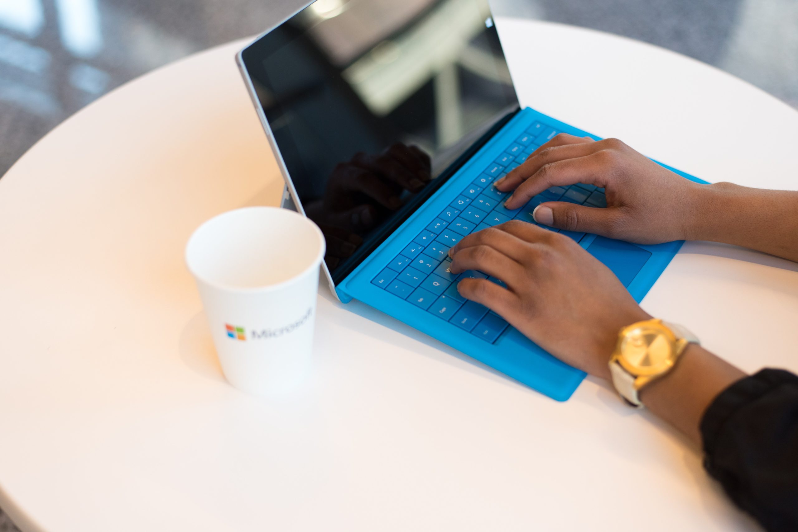 person-wearing-round-gold-colored-watch-using-Microsoft-Surface